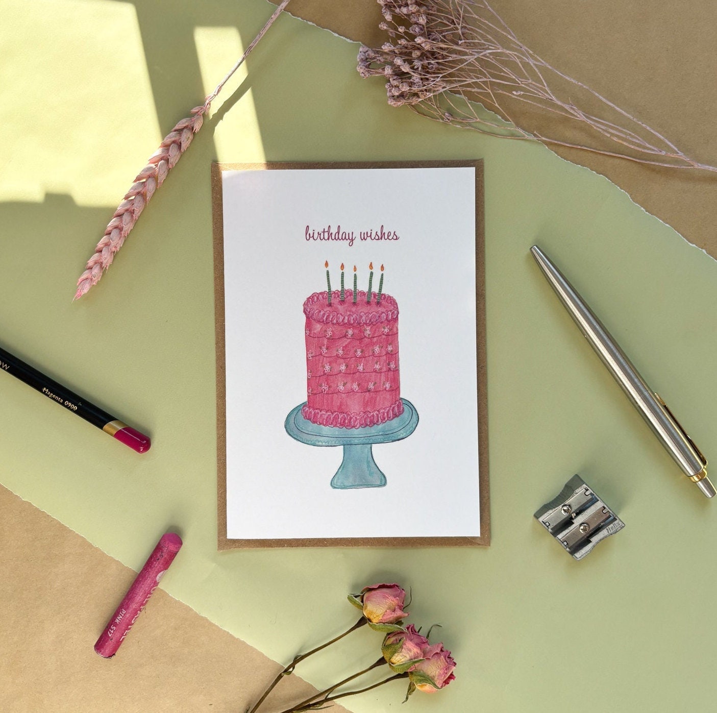 A birthday wishes greeting card featuring a pink illustrated cake and a birthday wishes message on the front