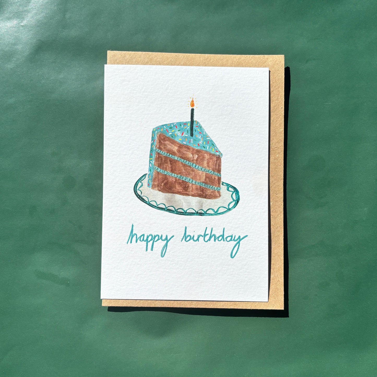 Greeting card featuring a slice of birthday cake with blue icing and sprinkles and 'happy birthday' text.