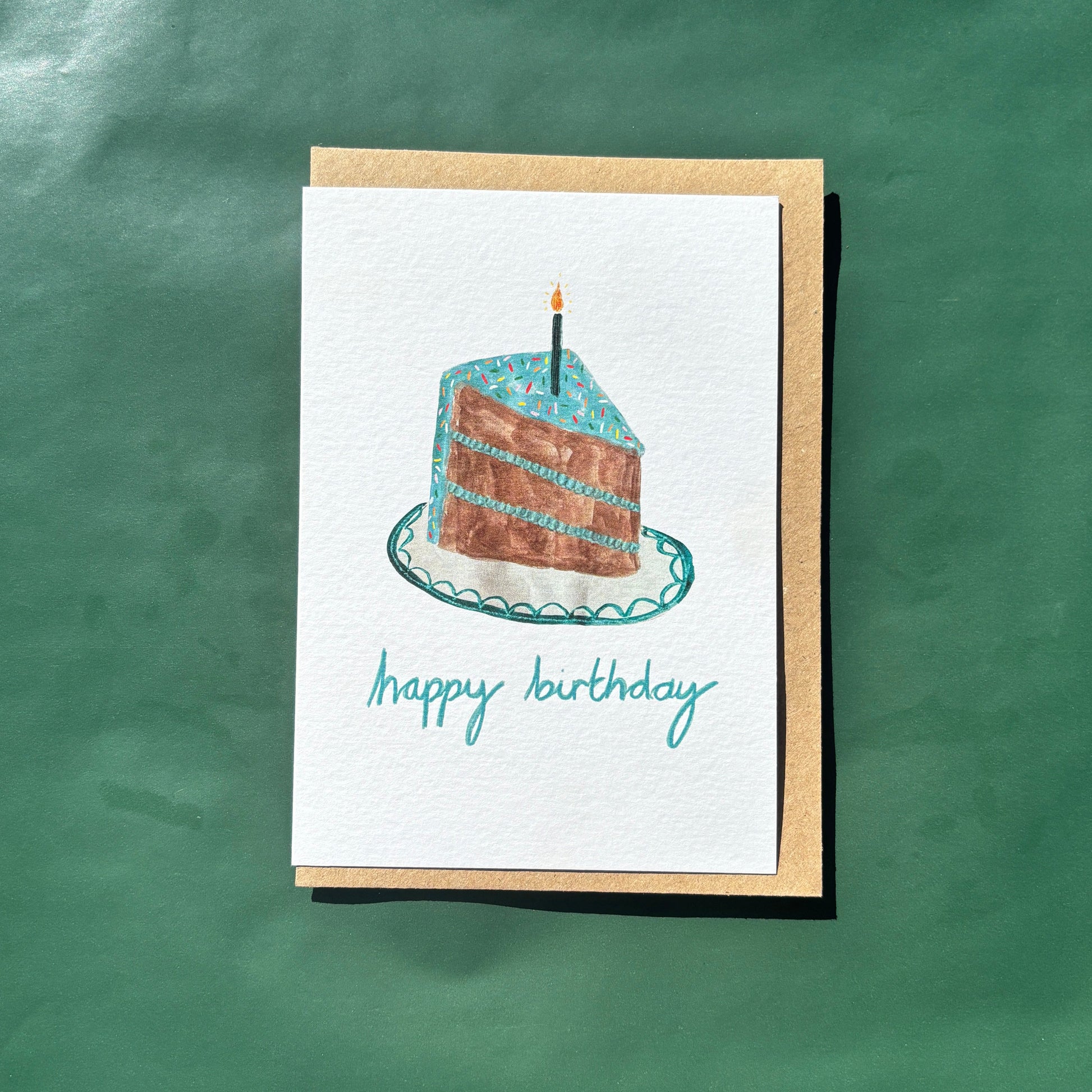 Greeting card featuring a slice of birthday cake with blue icing and sprinkles and 'happy birthday' text.