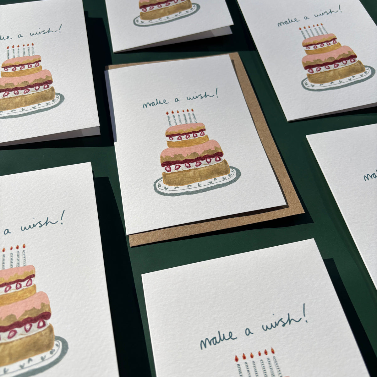 Multiple greeting cards with cake illustrations and text on a dark surface