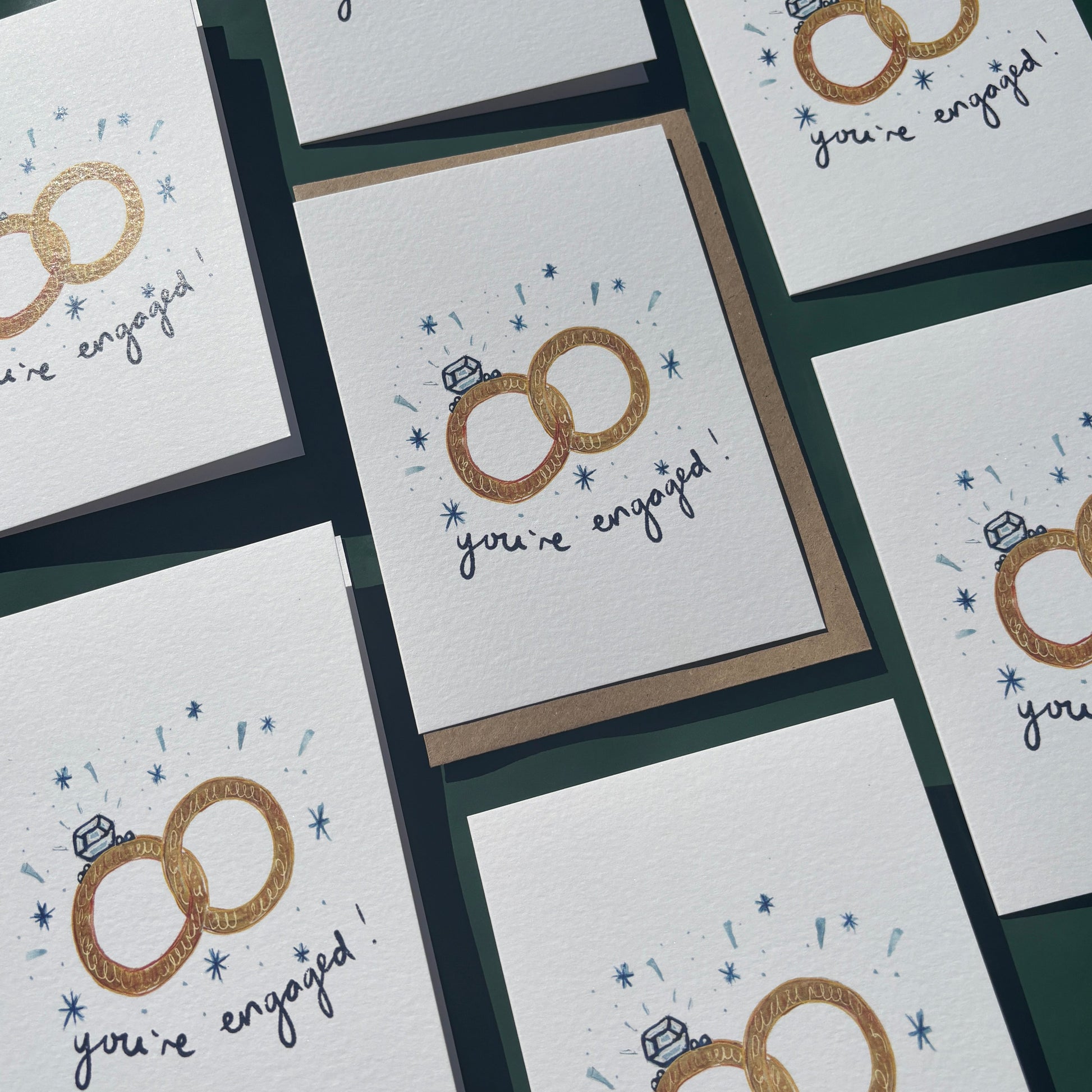 Multiple greeting cards with engagement ring illustrations and 'you're engaged text'.