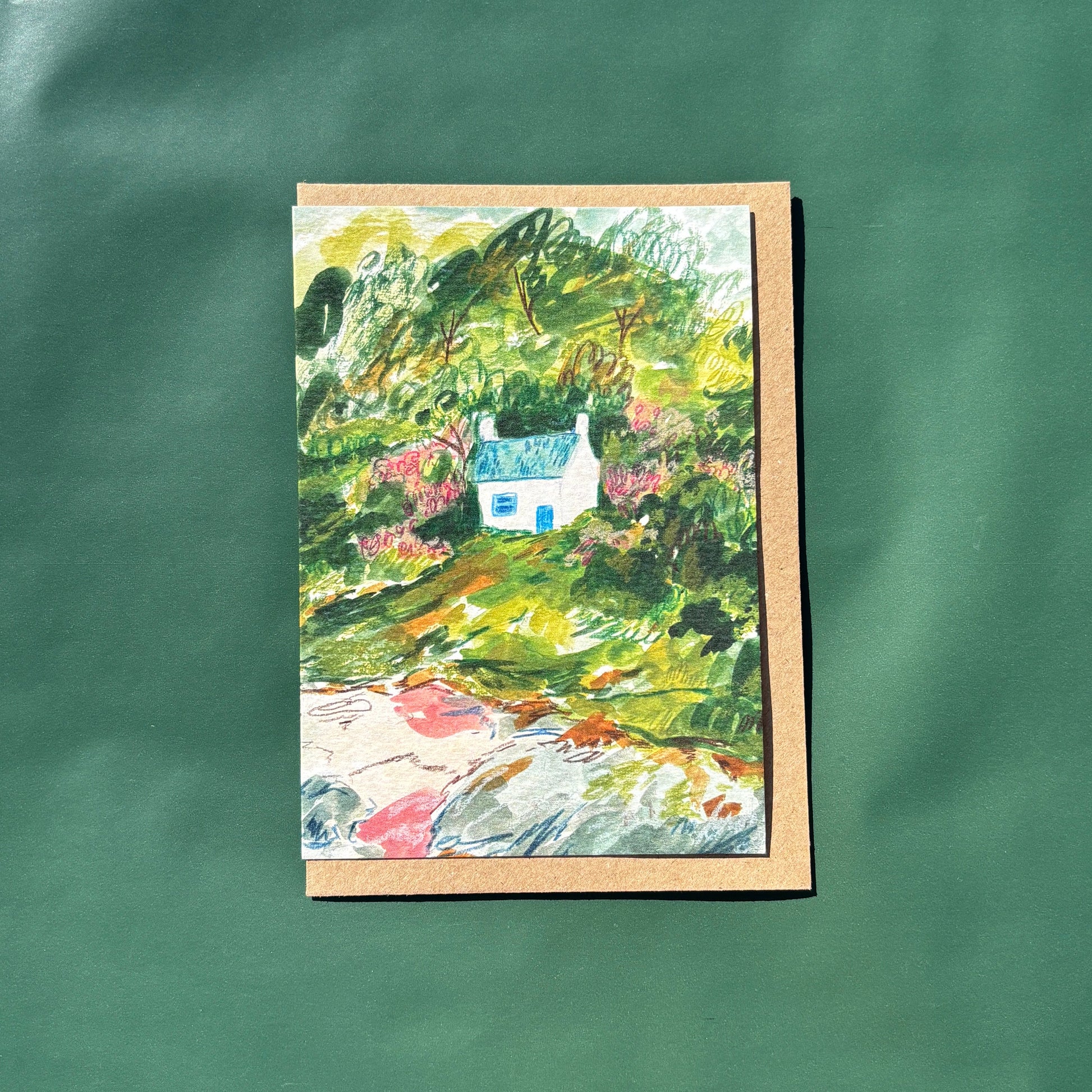 greeting card featuring a painting of a seaside cottage within a landscape with a brown envelope 