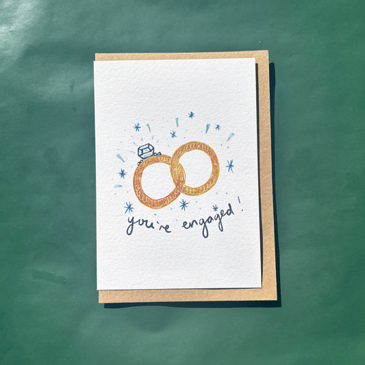 Greeting card featuring an illustration of engagement rings with 'you're engaged' text.